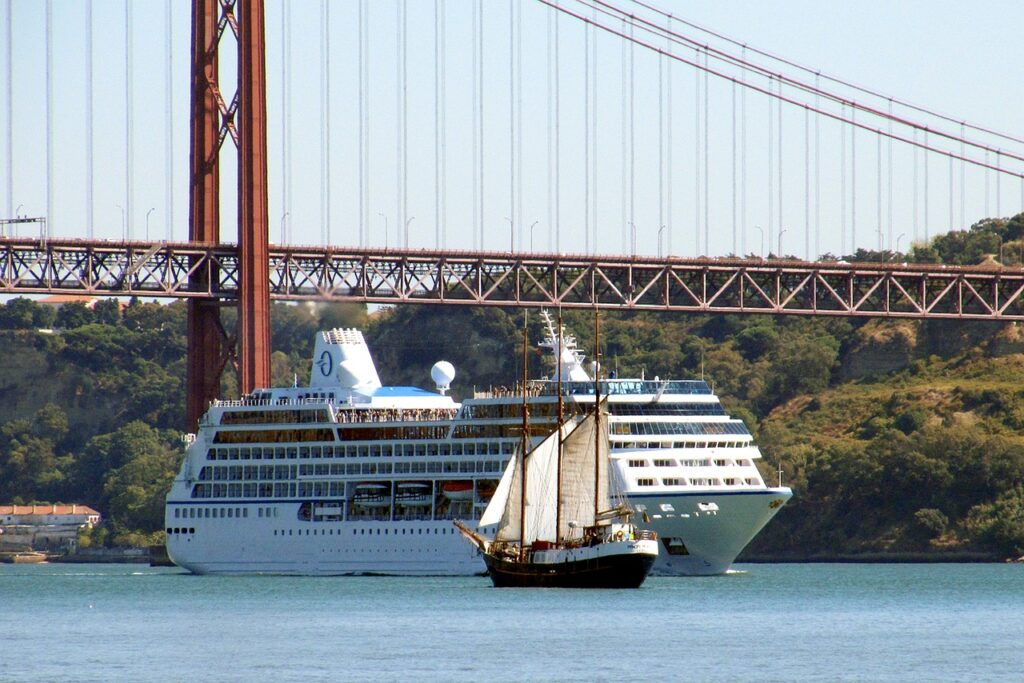 Small cruise ship going under a bridge and being passed by a sail boat.