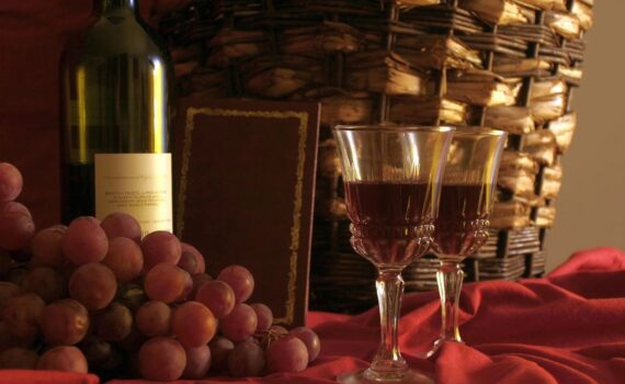 Bottle and glass of red wine surrounded by grapes.