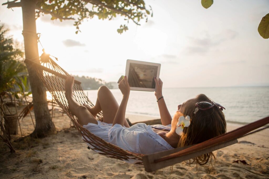 Woman in hammock on the beach with headphones and a tablet on a weekend getaway