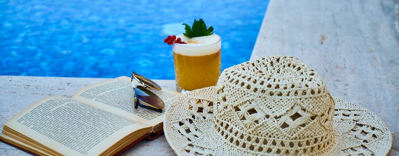 Drink, book and sun hat by a pool