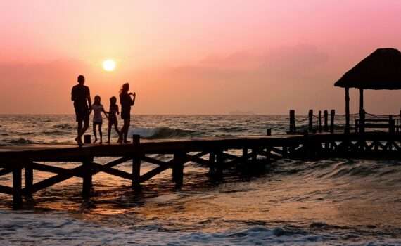 Pier on a beach at sunset with a family walking on it