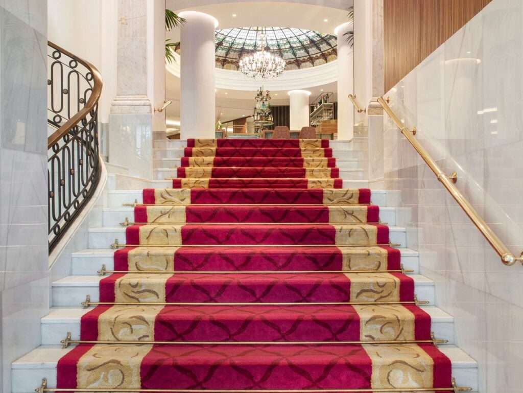 The grand stairs to the lobby of the Hotel Colon, a Gran Melia Property. Stairs are covered in a royal red carpet with gold trim.