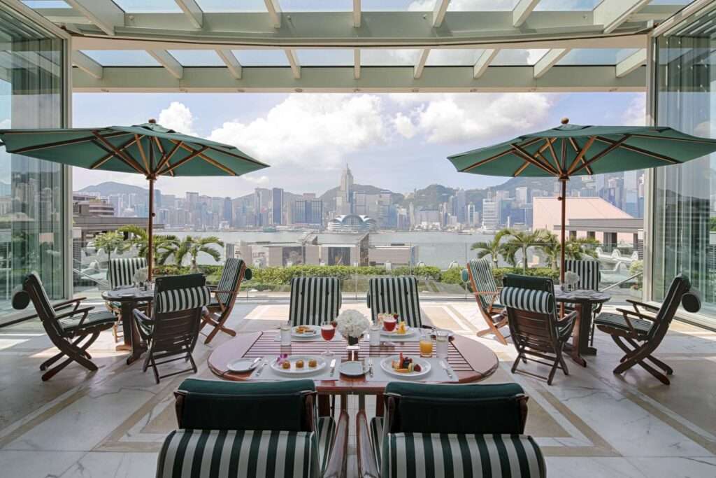 Poolside dining area at the Peninsula Hong Kong. Tables with umbrellas overlooking the pool with a back drop of mountains.