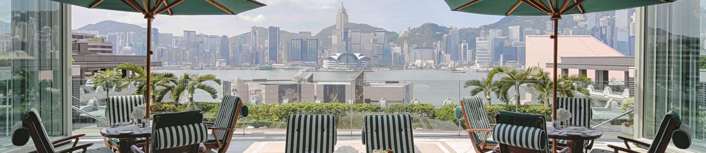 Poolside dining area at the Peninsula Hong Kong. Tables with umbrellas overlooking the pool with a back drop of mountains.