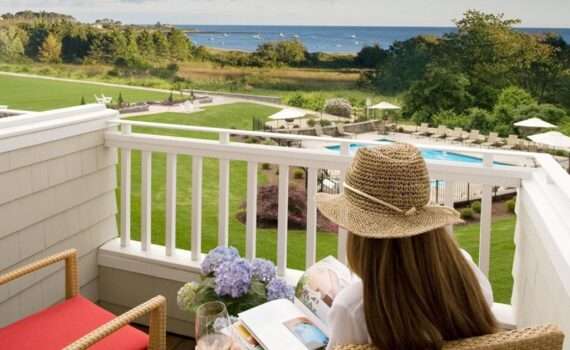 A woman sitting on a deck at Inn by the Sea. Reading a book with a view of the Ocean.