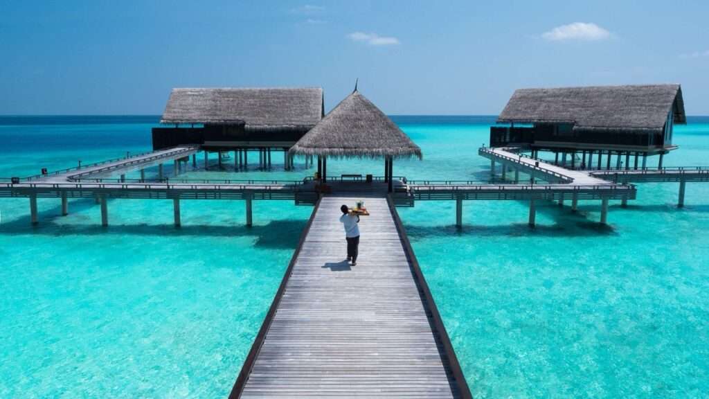 A pier going out over the clear blue ocean in the Maldives to overwater bungalows. One&Only Reethi Rah - a luxury hotel