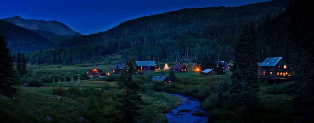 Dunton Hot Springs resort lit up at dusk with the mountains in the back drop - this is a luxury lodge in the USA