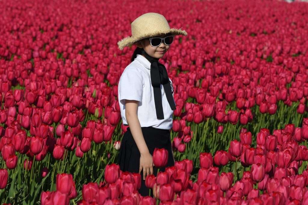 Girl with had and sun glasses standing in a field of red tulips at the Skagit Tulip Festival
