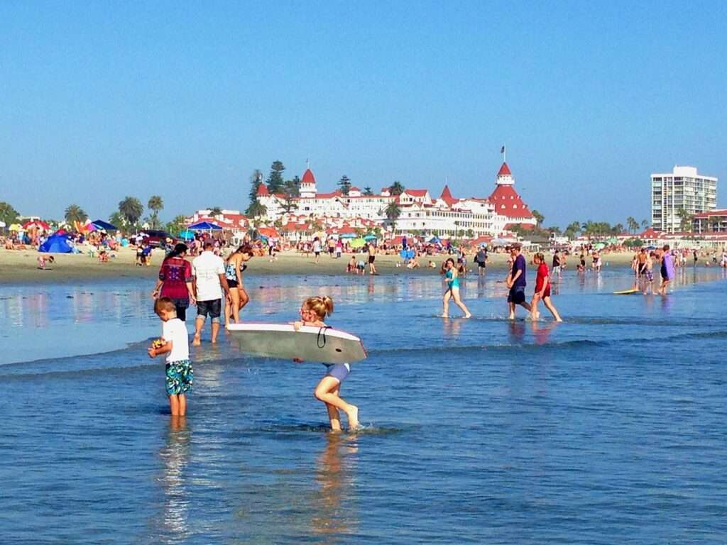 View of the Hotel Del Coronado from the water, with families swimming and playing on the beach