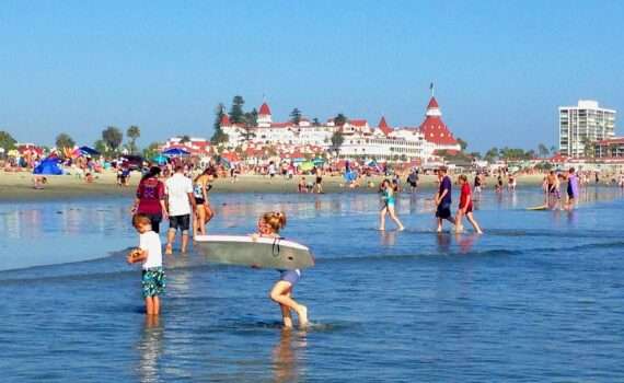 View of the Hotel Del Coronado from the water, with families swimming and playing on the beach