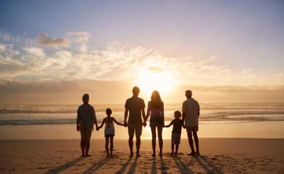 Multi-generational family holding hands and looking at the ocean at sunset