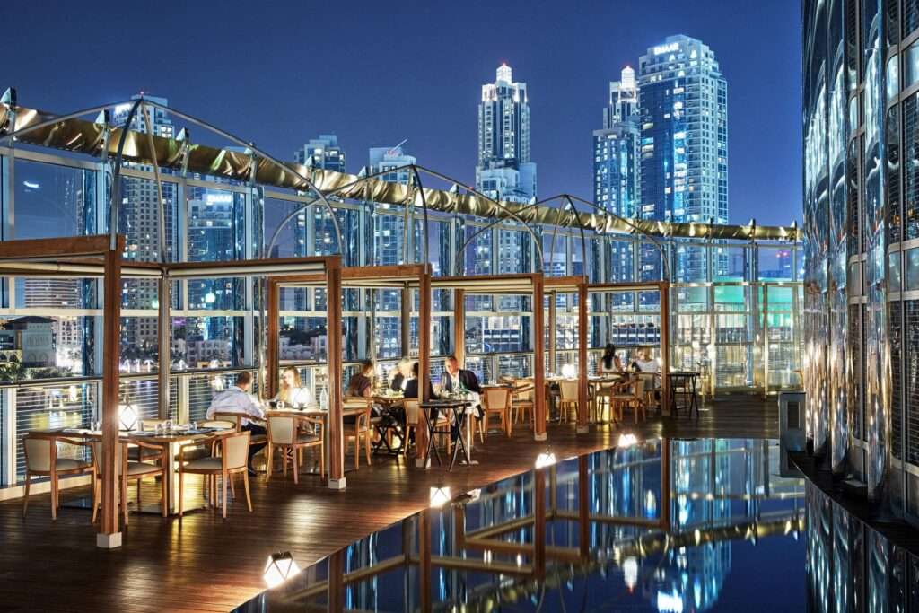 Armani Amal Terrace - view of the out door cafe at night with the city skyline behind the diners