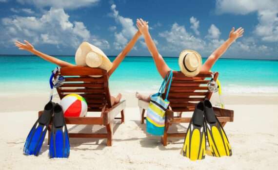 a couple sitting by the ocean with sun hats and stuff to pack for a cruise