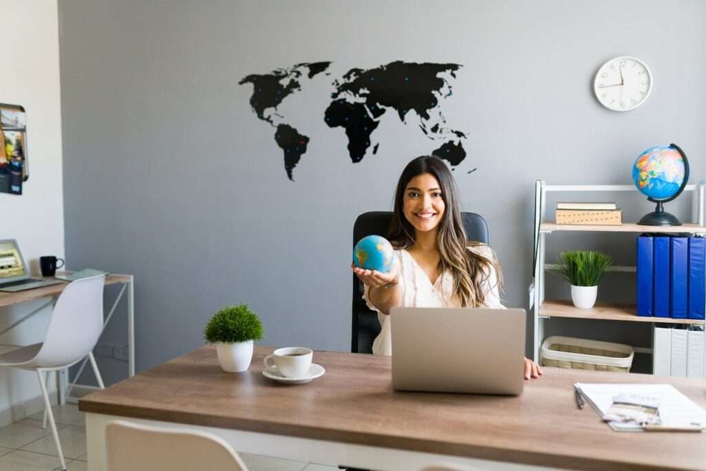 Luxury travel agent with a global map behind her and holding out a globe